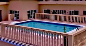 Una piscina rectangular con valla blanca y una planta pequeña en la esquina.