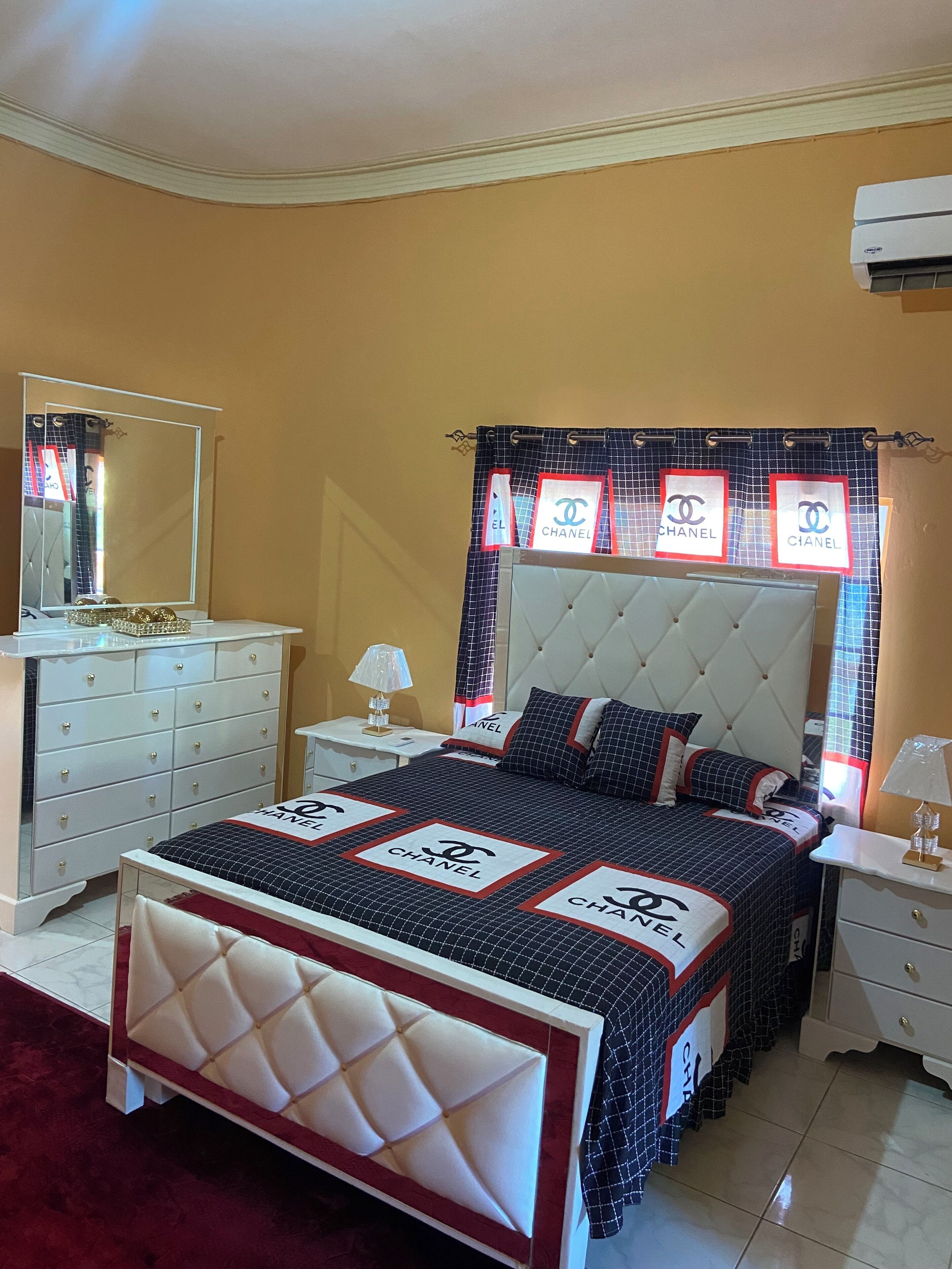 A bedroom with a bed, a dresser, a nightstand, a mirror, and a window with a curtain.