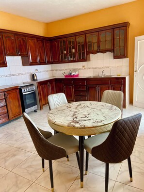 A kitchen with wooden cabinets, a stove, a sink, and a round marble table with four chairs. - Deluxe 1 Bedroom Apartment with Seaview and Swimming Pool (Rio Nuevo)