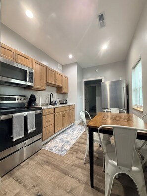 A modern kitchen with wooden cabinets, stainless steel appliances, and a dining area with a wooden table and chairs. - Fabulous 2-bedroom house with AC in charming Sandusky (Sandusky)