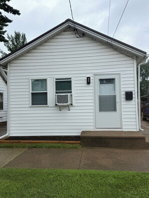 A single-story white building with a front door, two windows, and an air conditioning unit. - Fabulous 2-bedroom house with AC in charming Sandusky (Sandusky)