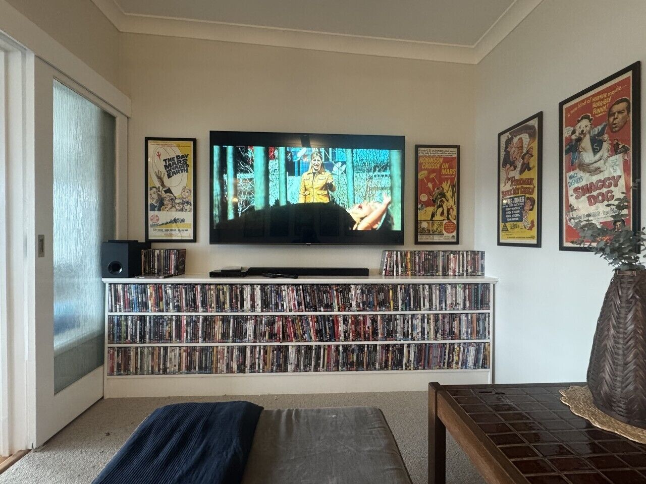 A living room with a flat-screen TV, a bookshelf filled with DVDs, and a coffee table.