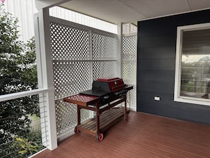 A covered outdoor area with a grill cart and a white lattice fence.