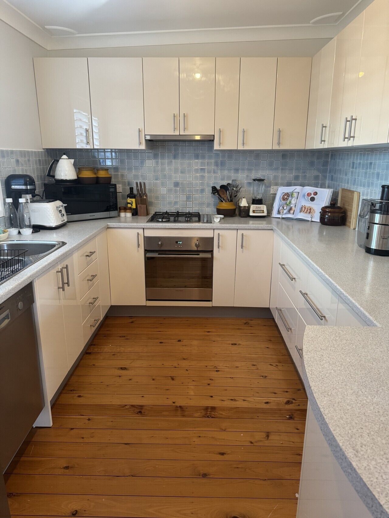 A modern kitchen with white cabinets, a stainless steel range, and a wooden floor.