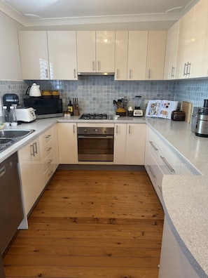 A modern kitchen with white cabinets, a stainless steel range, and a wooden floor. - Entire retro styled home in Mollymook Beach (Mollymook Beach)