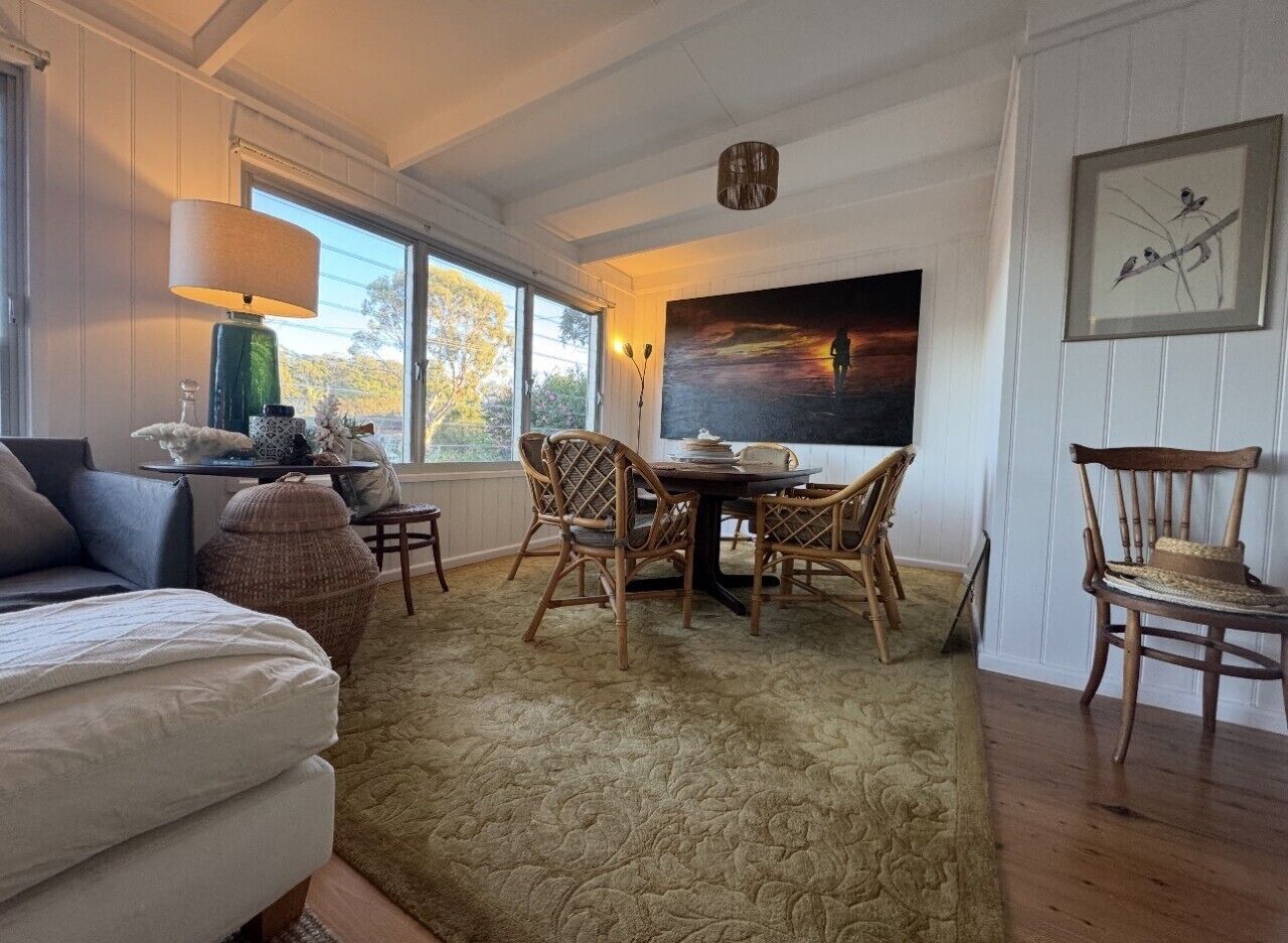 Un salon chaleureux avec un canapé, une table à manger et des chaises, une grande fenêtre et un tableau accroché au mur.