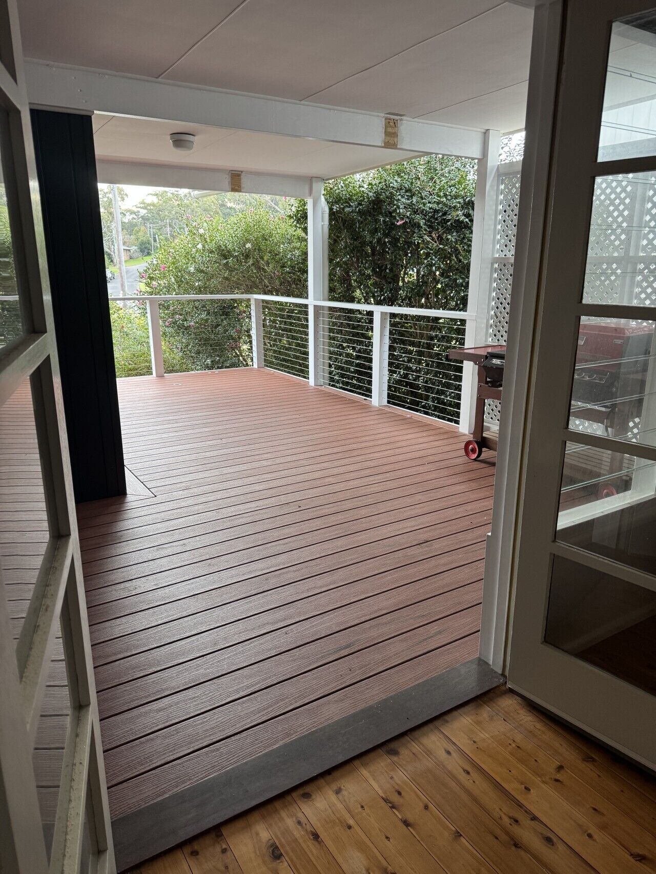 A covered outdoor area with a wooden deck, white railings, and a view of greenery.