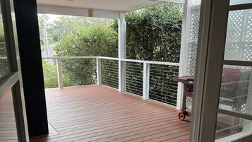 A covered outdoor area with a wooden deck, white railings, and a view of greenery.