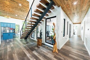 A modern interior with a wooden staircase, a kitchen area, and a large window. - The Revel | 24-Guest Luxury Cabin + Views (Broken Bow)