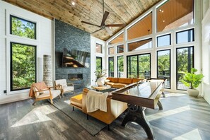 A spacious living room with a fireplace, large windows, and a pool table. - The Revel | 24-Guest Luxury Cabin + Views (Broken Bow)
