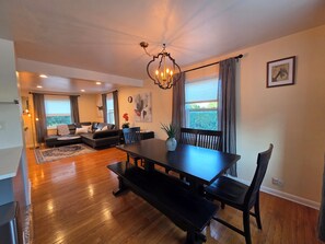 A spacious living area with a dining table, seating, and a view through large windows. - Luxury Cozy Stay-Near Six Flags, Navy Base (Gurnee)