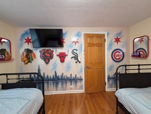 A room with two beds, a door, and a wall with sports team logos and a cityscape mural. - Luxury Cozy Stay-Near Six Flags, Navy Base (Gurnee)