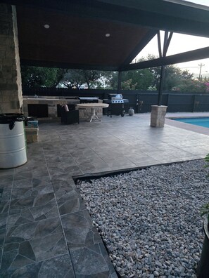 Eine Außenpatio-Terrasse mit einer Steingrillanlage, einem Pool und einem überdachten Sitzbereich.