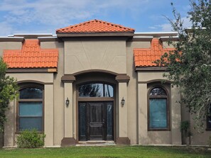 A two-story building with a symmetrical facade, featuring a central entrance with a dark door, flanked by two windows with shutters, and a tiled roof. - Spacious 5-bedroom house in marvelous San Juan Texas . Pet friendly home. 
. (San Juan)