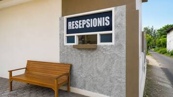 Un mostrador de recepción con un cartel que dice 'RESEPSIONIS' y un banco de madera en el exterior.