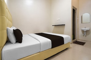 Un dormitorio moderno con cama, almohadas, mesita de noche, espejo y lavamanos.