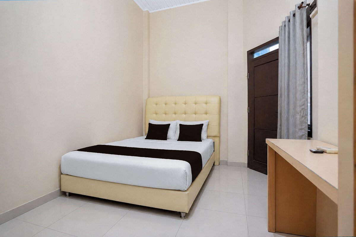 Una cama individual con cabecera, una mesita de noche y un armario en una habitación con paredes lisas y piso de baldosas.
