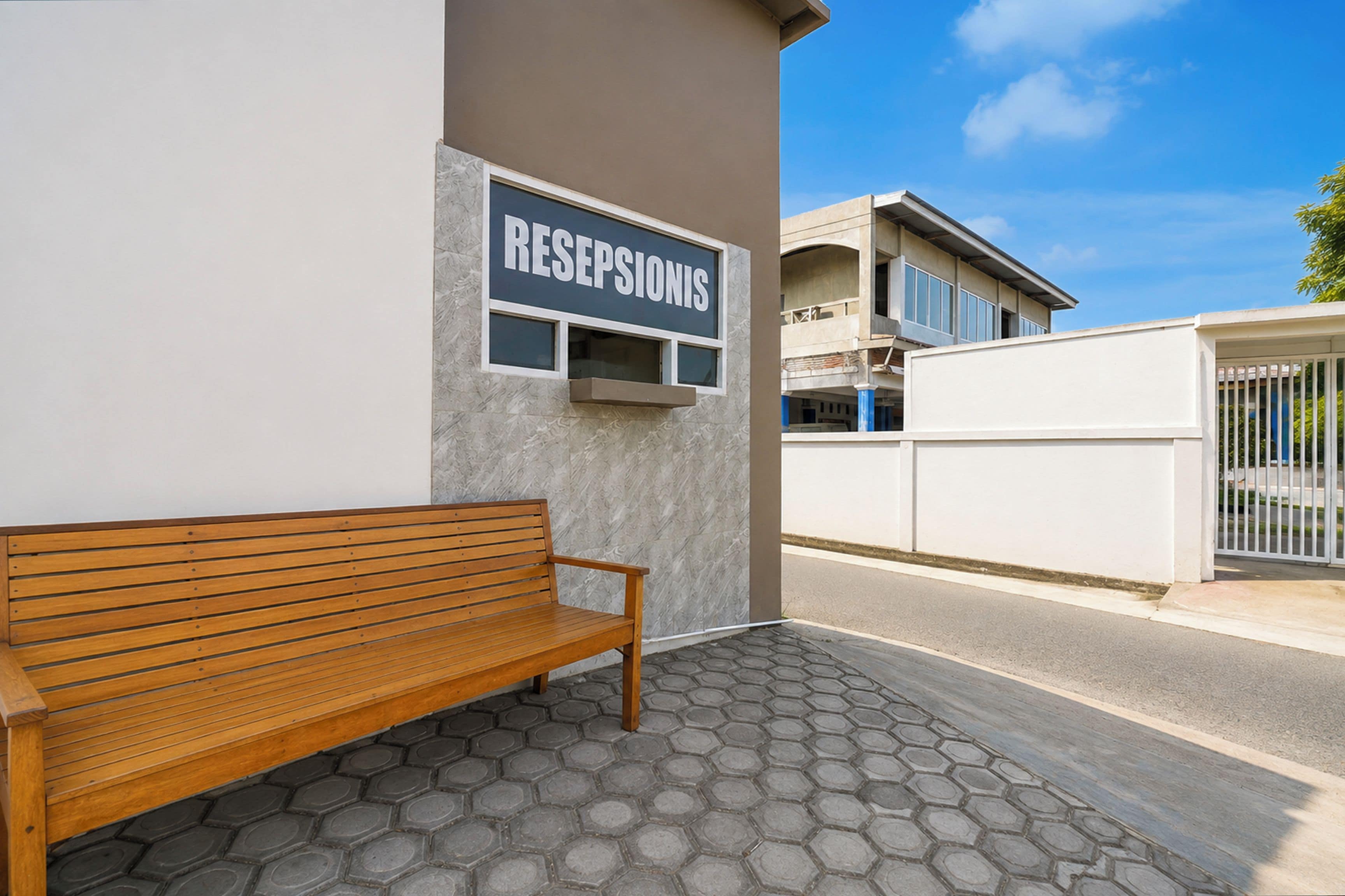 A reception area with a wooden bench, a sign reading 'RESEPSIONS', and a building in the background.