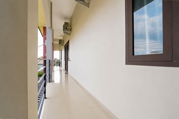 A corridor with a window on the right, a metal railing on the left, and a tiled floor.