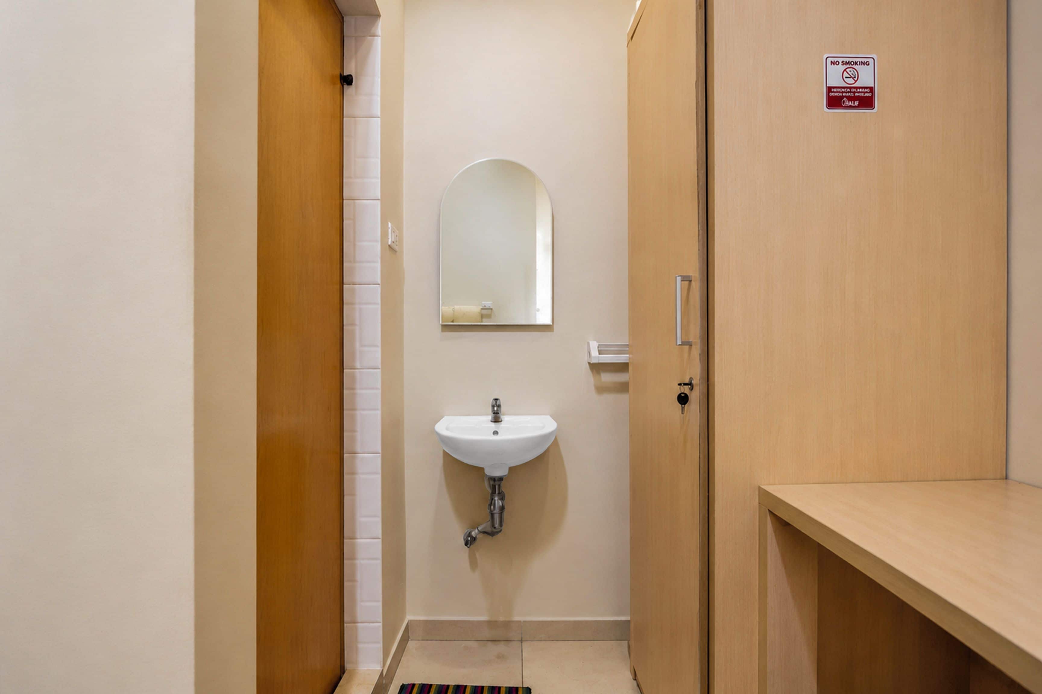 Un baño pequeño con un lavamanos blanco, un espejo y una puerta de madera.