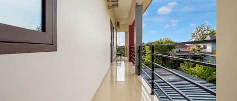 A clean, modern corridor with a shiny tiled floor, a metal railing on the right, and a clear view of the sky and greenery outside.