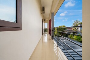 Un pasillo limpio y moderno con un suelo de baldosas brillantes, una barandilla metálica a la derecha y vistas despejadas al cielo y al verdor exterior.