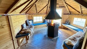 A cabin interior with a central wood-burning stove, wooden benches with fur throws, and a sloped ceiling. - Little Lake Lodge Retreat Sleeps 2 with Parking (Ballycastle)