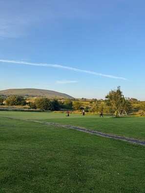 Ein grasbewachsenes Feld mit blauem Himmel, eine Hügelkette in der Ferne und einer Schaukel.