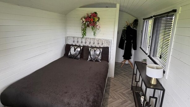 A bedroom with a bed, a dresser, a mirror, and a window with blinds. - Little Lake Lodge Retreat Sleeps 2 with Parking (Ballycastle)