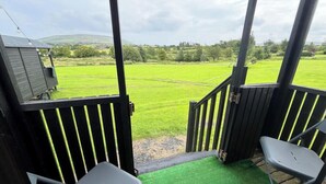 A covered outdoor area with a view of a green field, a small building, and a chair. - Little Lake Lodge Retreat Sleeps 2 with Parking (Ballycastle)
