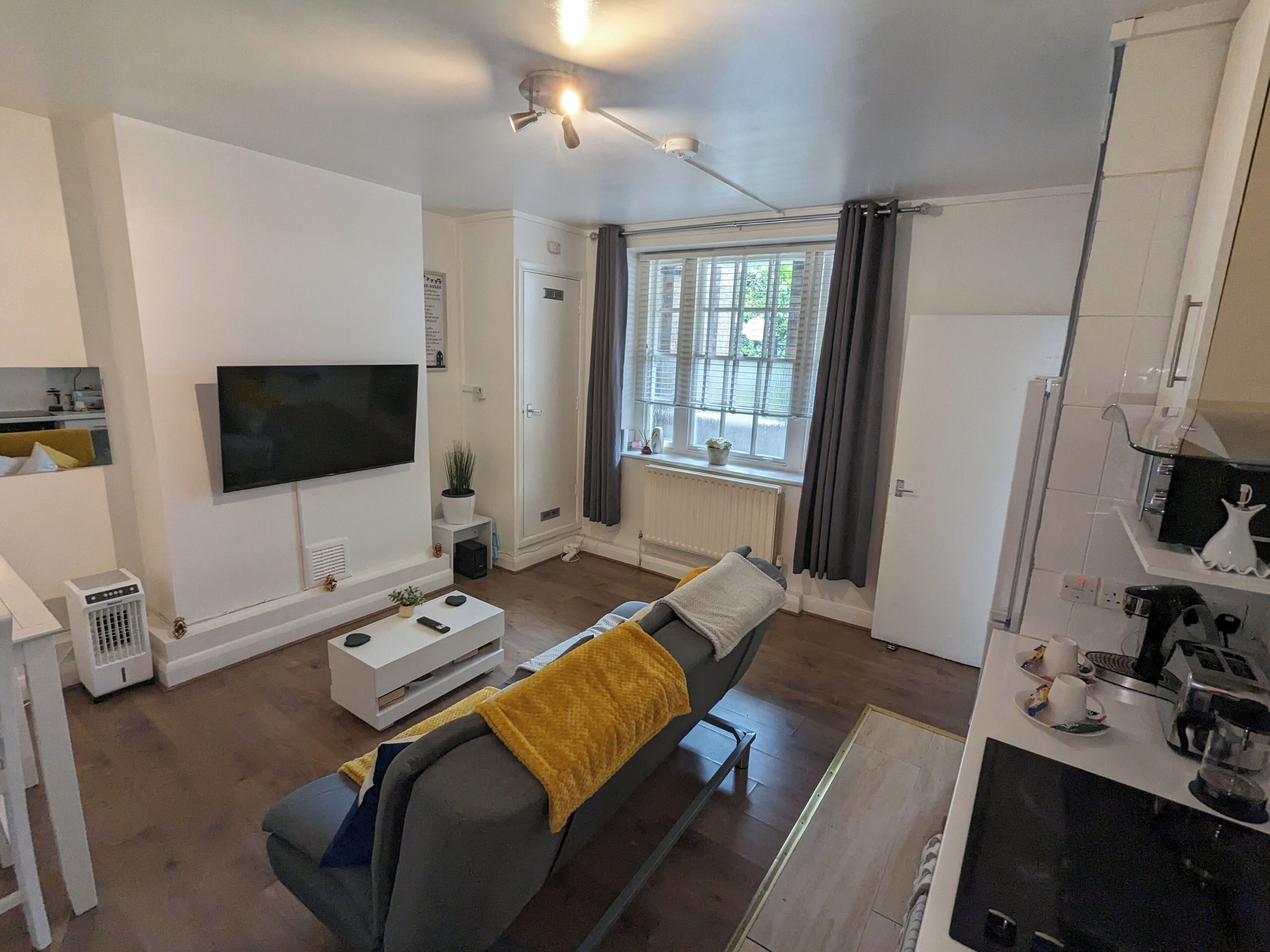 Een moderne woonkamer met een bank, een flatscreen-tv, een plafondventilator en een raam met gordijnen.