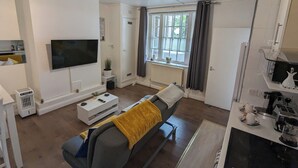 Een moderne woonkamer met een bank, een flatscreen-tv, een plafondventilator en een raam met gordijnen.