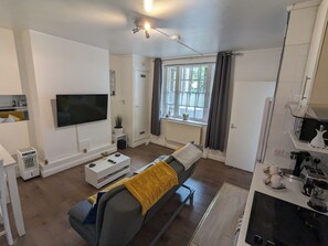 Ein modernes Wohnzimmer mit einer Couch, einem Flachbildfernseher, einem Deckenventilator und einem Fenster mit Vorhängen.