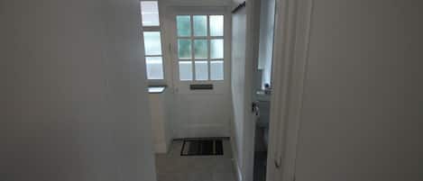 A narrow hallway with a door at the end, leading to a room with a window.