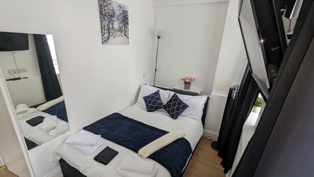 Hotelkamer met een bed, een spiegel, een schilderij, een nachtkastje met een lamp en een potplant.