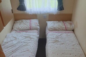Una habitació petita i tancada amb dos llits individuals, cadascun amb un llençol blanc i dibuixos de punts i vora rosa.
