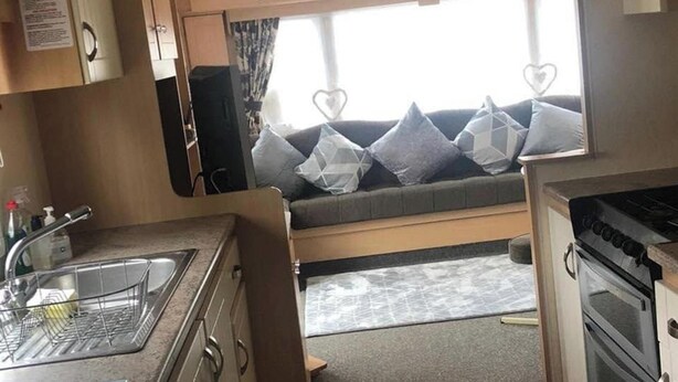 A compact RV interior with a kitchenette, a sofa with heart-shaped cushions, and a window with curtains. - 10 Berth Caravan Butlins Skegness Pet friendly (Skegness)