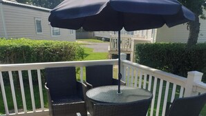 A balcony with wicker chairs and a table, a white railing, and a view of a lawn and a house in the background. - 10 Berth Caravan Butlins Skegness Pet friendly (Skegness)