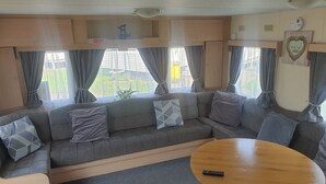 A cozy RV interior with a sofa, a wooden table, and curtains. - 10 Berth Caravan Butlins Skegness Pet friendly (Skegness)