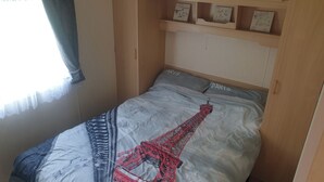 A bedroom with a bed featuring a Paris-themed design, a wooden wardrobe, and a window with a curtain. - 10 Berth Caravan Butlins Skegness Pet friendly (Skegness)