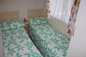 A small, single-room accommodation with two single beds, a bedside table, and a window with curtains. - 10 Berth Caravan Butlins Skegness 2 showers pets (Skegness)