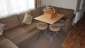A living room with a brown sofa, a small table, and two bar stools. - 10 Berth Caravan Butlins Skegness 2 showers pets (Skegness)