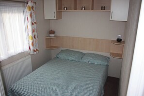 A small bedroom with a single bed, a window with curtains, and a shelf with jars. - 10 Berth Caravan Butlins Skegness 2 showers pets (Skegness)