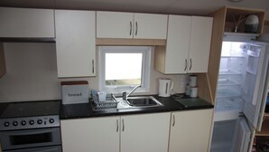 A compact kitchen with white cabinets, a built-in oven, a sink, and a window above the countertop. - 10 Berth Caravan Butlins Skegness 2 showers pets (Skegness)
