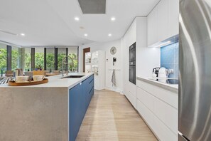 A modern kitchen with a large island, built-in appliances, and a view of greenery outside. - Luxury 3-bedroom Penthouse Apartment (Casuarina)