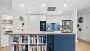 Una cocina moderna con armarios blancos, una pared de acento azul y una estantería empotrada con libros.