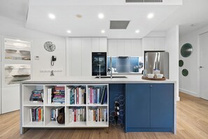 Eine moderne Küche mit weißen Schränken, einer blauen Akzentwand und einer eingebauten Bücherregal mit Büchern.