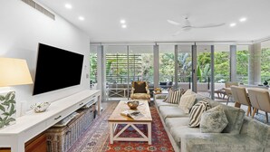 Una sala de estar moderna con televisor de pantalla plana, un sofá, una mesa de centro y un ventanal con vistas a la vegetación.