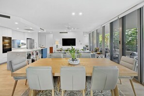 A modern kitchen with white cabinets, a built-in oven, and a dining area with a wooden table and grey chairs. - Luxury 3-bedroom Penthouse Apartment (Casuarina)