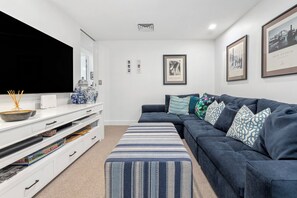 A modern living room with a sectional sofa, a flat-screen TV, a console table with decorative items, and framed artwork on the walls. - Luxury 3-bedroom Penthouse Apartment (Casuarina)